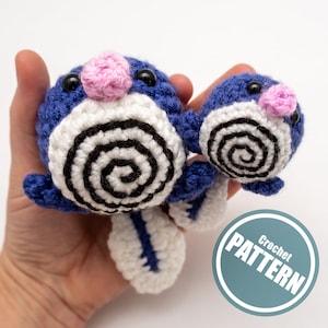 May include: Two crocheted blue and white amigurumi plushies with black eyes and pink noses. The plushies are in the shape of a cartoon character with a spiral pattern on the front. The plushies are being held in a hand. The image also includes a blue circle with the text "Crochet PATTERN" in white.