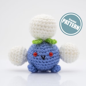 May include: Crocheted blue and white amigurumi toy with a green leaf and red eyes. The toy is a representation of a Pokemon character. The image includes the text "Crochet PATTERN".