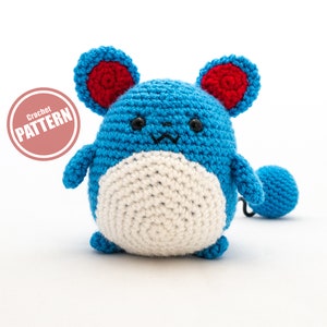 May include: Crocheted blue and white plush toy with red ears. The toy is shaped like a small animal with a round body and a long tail. The text "Crochet PATTERN" is visible in the image.
