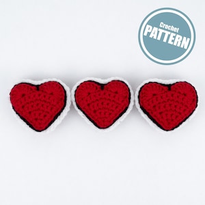 May include: Three red crocheted hearts with white and black edging on a white background. A blue circle with the text "Crochet Pattern" is in the top right. The hearts are evenly spaced.