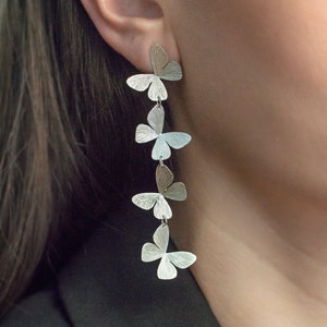 May include: Silver butterfly earrings with five butterfly charms hanging from a single hook. The earrings are long and dangle.