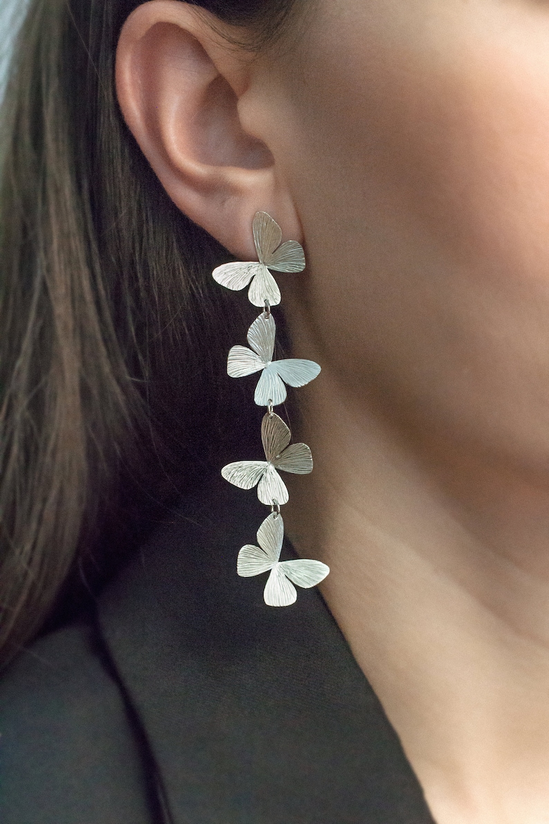 May include: Silver butterfly earrings with five butterfly charms hanging from a single hook. The earrings are long and dangle.