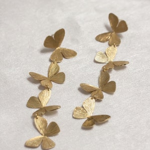 May include: A pair of gold butterfly dangle earrings with multiple butterfly charms hanging from each earring.