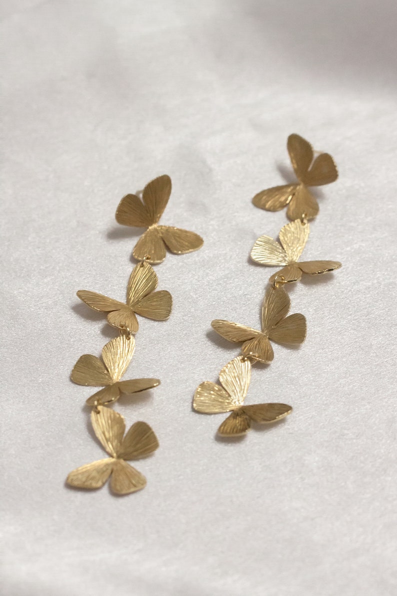 May include: A pair of gold butterfly dangle earrings with multiple butterfly charms hanging from each earring.