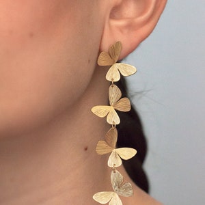 May include: Gold butterfly earrings with five butterflies dangling from each other. The butterflies are textured and have a slightly hammered look.