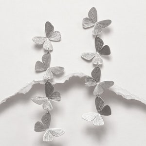 May include: Silver butterfly earrings with multiple butterfly charms hanging from each earring.
