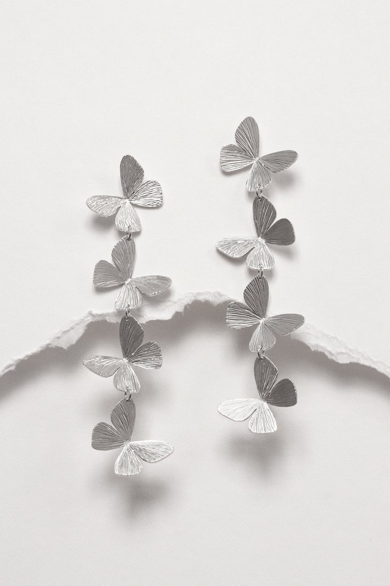 May include: Silver butterfly earrings with multiple butterfly charms hanging from each earring.