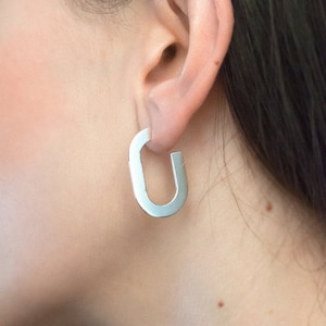 Puede incluir: Pendientes de aro de plata con una forma ovalada única. Los pendientes son simples y modernos, y serían una gran adición a cualquier colección de joyas.