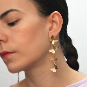 May include: Gold butterfly earrings with multiple butterfly charms hanging from a single post. The earrings are long and dangle.