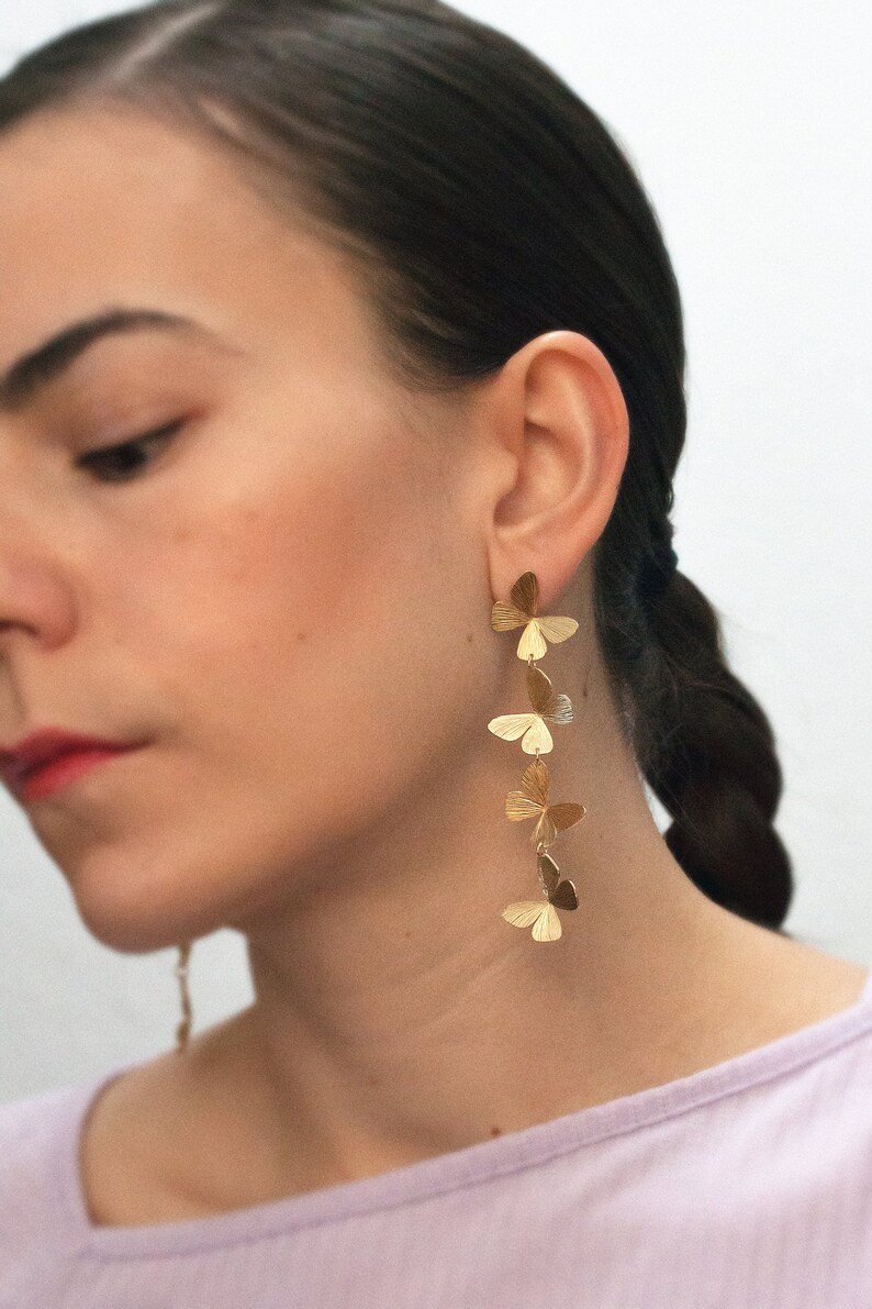 May include: Gold butterfly earrings with multiple butterfly charms hanging from a single post. The earrings are long and dangle.
