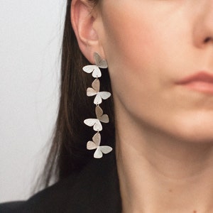 May include: Silver butterfly earrings with a layered design. The earrings are long and dangle from the earlobe.