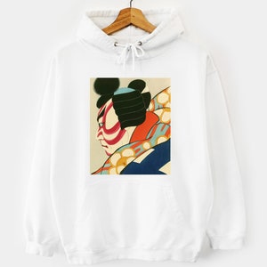 Op de afbeelding: Witte hoodie met een vierkante afbeelding van een Japanse Kabuki-acteur. De afbeelding toont een profiel van het gezicht van de acteur met rode en witte make-up, zwart haar en kleurrijke kleding. De hoodie heeft een capuchon met trekkoord en een voorzak.