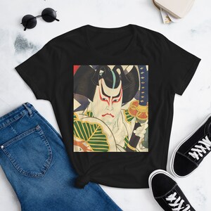 以下が含まれることがあります： 剣を持った侍のカラフルなイラストが描かれた黒いTシャツ。侍は緑と金の伝統的な日本の衣装を着ています。