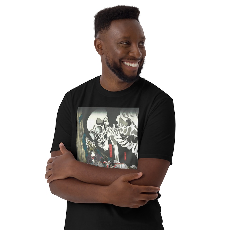 May include: Black t-shirt featuring a detailed, vintage Japanese woodblock print. The artwork depicts two skeletons, one with a large skull, and a figure in traditional clothing. The print has a dark, gothic aesthetic.