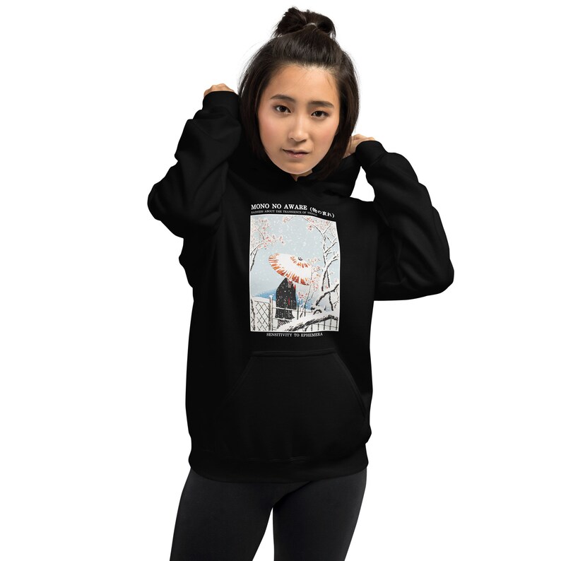 May include: Black hoodie featuring a Japanese-inspired print. The print depicts a person with an umbrella in a snowy landscape, with text that reads "MONO NO AWARE" and "SENSITIVITY TO EPHEMERA". The hoodie has a front pocket and a drawstring hood.