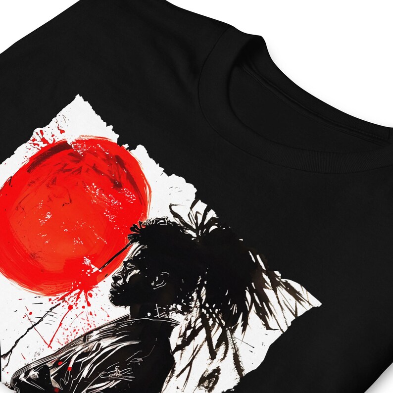 May include: Black t-shirt featuring a striking graphic design. The design includes a large red circle, a black silhouette of a person, and white and red accents. The artwork has a bold, artistic style.