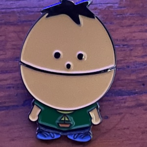 May include: A yellow cartoon character with black hair, green shirt, and blue shoes. The character has a surprised expression and is wearing a small sailboat on their shirt.