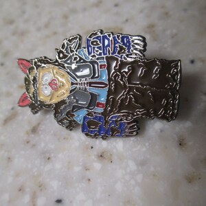 May include: A brown and blue enamel pin featuring a cartoon character with a wolf-like head and a human body. The character is wearing a blue shirt with a white collar and a red tie. The pin has the text "GERMS" on the top and "CITY" on the bottom.