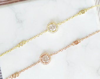 May include: Two delicate bracelets with a round, clear crystal centerpiece surrounded by smaller crystals. One bracelet is gold and the other is rose gold.