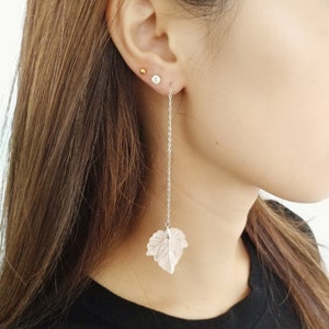 Könnte beinhalten: Silberne Ohrringe mit einem Blattdesign. Die Ohrringe sind lang und haben eine zarte Kette.