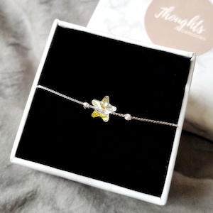 May include: A silver chain bracelet with a star-shaped charm. The charm is a clear crystal with yellow and green hues. The bracelet is presented in a white box with a black interior. The box has a logo that says "Thoughts Accessories".
