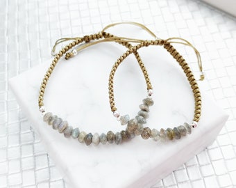 May include: Two adjustable bracelets with brown cord and silver beads, each with a row of grey labradorite stones.