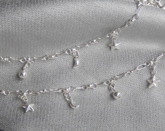 May include: Two silver anklets with charms. Each anklet has a crescent moon, a star, and a small ball charm.