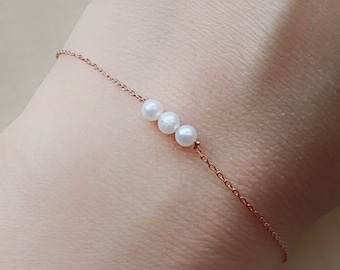 May include: A delicate gold chain bracelet with three white pearls.