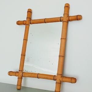 May include: A rectangular wall mirror featuring a frame constructed from light brown bamboo-style wood. The frame consists of four segments joined at the corners, with the ends of the bamboo extending past the joints. The mirror glass shows signs of age.