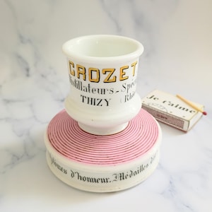 K&ouml;nnte beinhalten: Eine wei&szlig;e Keramiktasse mit schwarzem Henkel und dem Text "But First, Coffee" in handschriftlichem Stil. Die Tasse steht auf einer wei&szlig;en Oberfl&auml;che. Die Tasse ist 10 cm hoch.