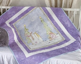 May include: A square quilt featuring a central illustration of two snowmen standing in a snowy landscape with trees, framed by a white border and a wide lavender purple patterned border. The quilt is draped over a white crib with a gray pillow.