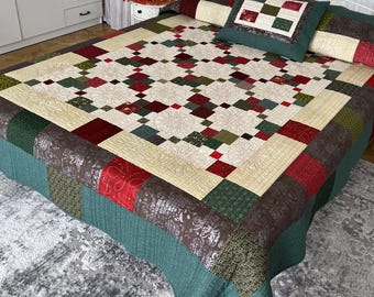 May include: A patchwork quilt featuring a grid of cream, dark red, forest green, and brown fabric squares with intricate floral and scroll patterns. The quilt is draped over a bed with a matching square pillow featuring a nine-patch center design.