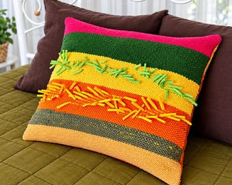 May include: A square throw pillow featuring horizontal stripes in hot pink, dark green, yellow, orange, and light orange. The yellow and orange sections are embellished with protruding, textured yarn loops in bright green and yellow.
