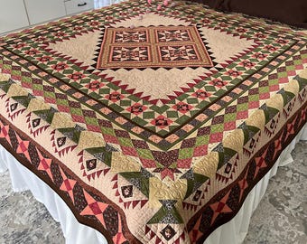 May include: A large, rectangular patchwork quilt featuring a central square block surrounded by intricate geometric patterns in shades of cream, olive green, dark brown, and muted red. The quilt has a quilted texture and a decorative border.