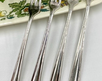 May include: Four silver-plated forks with ornate handles. The forks are arranged in a row on a white surface.