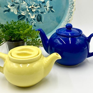 May include: Two ceramic teapots, one yellow and one blue. The yellow teapot has a lid with a small handle. The blue teapot has a traditional design.