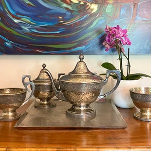 May include: A silver tea set with a teapot, creamer, sugar bowl, and a matching cup. The set has a hammered finish and intricate details.