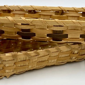 May include: Two woven oval baskets made of natural brown and light brown reeds. The baskets are stacked on top of each other.