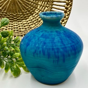 May include: A small, blue ceramic vase with a wavy, textured surface. The vase has a round body and a narrow neck.
