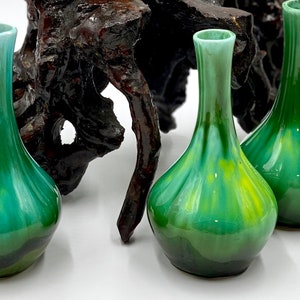 May include: Three small green and yellow ceramic vases with a glossy finish. The vases are arranged on a dark brown wooden surface.