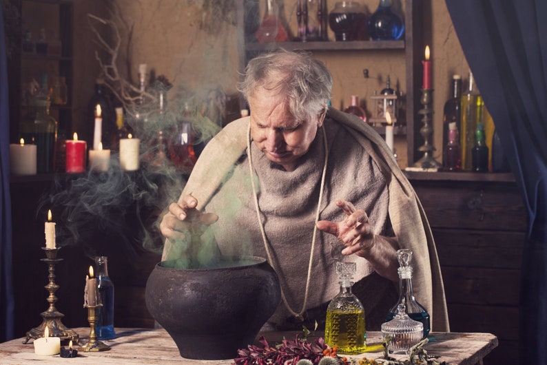 May include: An older man in a brown robe stirs a cauldron with a green liquid and smoke rising from it. He is surrounded by candles, bottles, and other potion-making supplies.