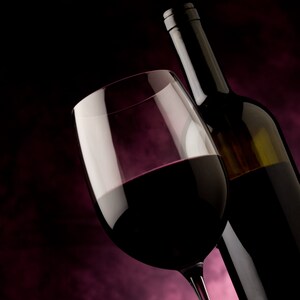 May include: A glass of red wine with a bottle of red wine in the background. The glass is full of wine and the bottle is partially visible.