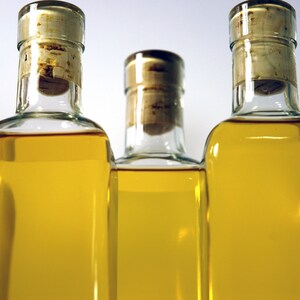 May include: Five clear glass bottles with cork tops filled with a golden yellow liquid. The bottles are arranged in a row, with the cork tops facing the viewer.