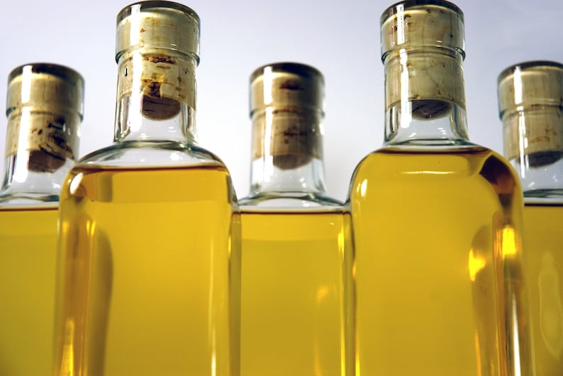 May include: Five clear glass bottles with cork tops filled with a golden yellow liquid. The bottles are arranged in a row, with the cork tops facing the viewer.