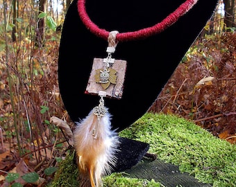 Op de afbeelding: Een handgemaakte sieradenset met een rode touwketting, bijpassende oorbellen en een hanger met een sleutel- en veerketting. De hanger en oorbellen hebben een houtachtige textuur met een uilontwerp. De set wordt op een zwarte standaard gepresenteerd.
