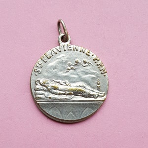 Puede incluir: Pendiente de plata con una inscripción dorada que dice "S.P.L.A.V.I.E.N.N.E. P.P.N." y una representación de una persona acostada.