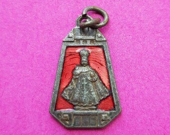May include: A silver pendant with a red enamel background and a silver image of a person wearing a robe. The pendant has a loop at the top for attaching to a chain.