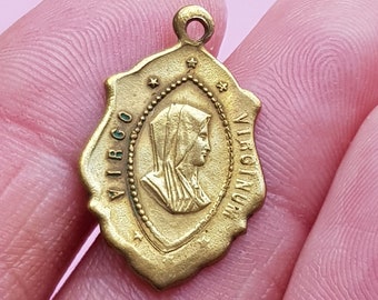 May include: A gold-colored metal pendant with a depiction of the Virgin Mary. The pendant is oval-shaped and has a loop at the top for hanging. The inscription "VIRGO" and "VIRGINIA" are visible on the pendant.