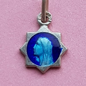 Puede incluir: Un colgante de plata con un diseño en forma de estrella de esmalte azul que presenta una imagen blanca de la Virgen María.