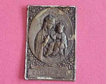 May include: A silver-toned metal religious pendant featuring a relief image of the Virgin Mary and baby Jesus. The pendant is surrounded by a floral design and has the inscription "B.V. DELLA CONSOLATA".